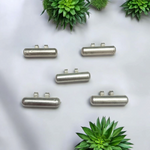 Five silver-plated cylindrical taweez amulets with accompanying Bhojpatra sheets placed neatly on a white surface