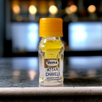 Glass bottle of 2ML Chameli Attar by Veena, adorned with a golden cap and floral-themed label, surrounded by jasmine flowers on a wooden surface