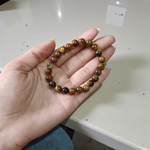 Image of a natural Tiger Eye bracelet made of 8mm golden-brown beads with a silky shine, arranged in a circular shape on a neutral background
