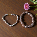 Image of two adjustable spiritual bracelets – one made with white Vaijanti seeds and the other with brown Kamal Gutta beads – displayed on a natural surface