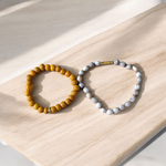 Image of two stretchable bracelets – one made with white Vaijanti seeds and one with yellow Haldi beads – arranged side by side on a natural background