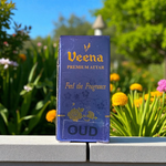 2ML glass bottle of OUD Attar by Veena, featuring a sleek gold cap and minimalist label, placed on a dark wooden surface with pieces of agarwood