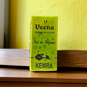 A 2ML bottle of Kewra Attar by Veena placed next to Kewra flowers, highlighting its traditional use in meditation and worship