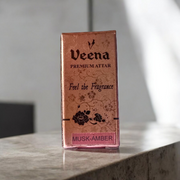 A 2ML roll-on bottle of Veena’s Musk Amber Attar placed elegantly with natural ingredients in the background, showcasing luxury and tradition
