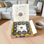 A box of MALAWALA Premium Cup Sambrani containing 12 natural dhoop cups arranged neatly, with one cup lit and emitting aromatic smoke