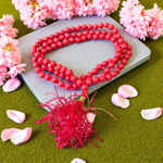 A handcrafted Lal Moonga Mala with 108+1 round red coral beads (6mm), used for puja and meditation, laid out on a spiritual backdrop