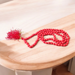 A handcrafted Lal Moonga Mala with 108+1 round red coral beads (6mm), used for puja and meditation, laid out on a spiritual backdrop