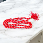 A handcrafted Lal Moonga Mala with 108+1 round red coral beads (6mm), used for puja and meditation, laid out on a spiritual backdrop