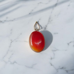 A handcrafted Natural Carnelian and Orange Aventurine pendant in sterling silver setting, displayed on a wooden background