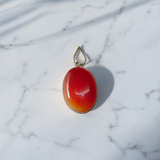 A handcrafted Natural Carnelian and Orange Aventurine pendant in sterling silver setting, displayed on a wooden background