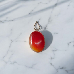 A handcrafted Natural Carnelian and Orange Aventurine pendant in sterling silver setting, displayed on a wooden background