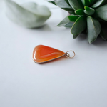A handcrafted Natural Carnelian and Orange Aventurine pendant in sterling silver setting, displayed on a wooden background