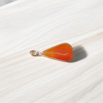 A handcrafted Natural Carnelian and Orange Aventurine pendant in sterling silver setting, displayed on a wooden background