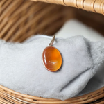 A handcrafted Natural Carnelian and Orange Aventurine pendant in sterling silver setting, displayed on a wooden background