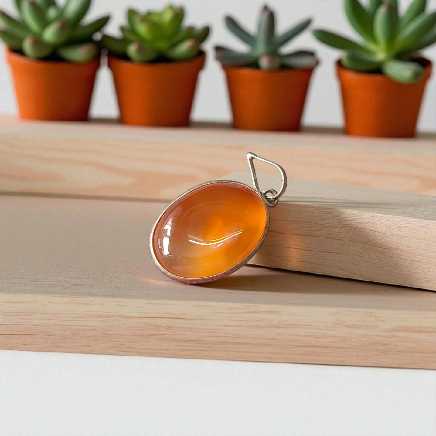 A handcrafted Natural Carnelian and Orange Aventurine pendant in sterling silver setting, displayed on a wooden background