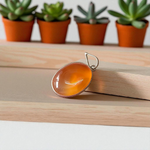 A handcrafted Natural Carnelian and Orange Aventurine pendant in sterling silver setting, displayed on a wooden background