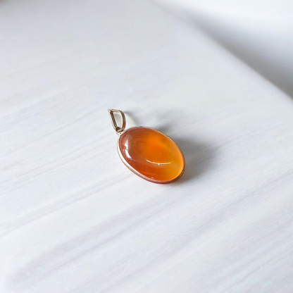 A handcrafted Natural Carnelian and Orange Aventurine pendant in sterling silver setting, displayed on a wooden background