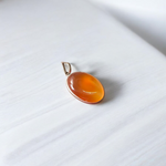 A handcrafted Natural Carnelian and Orange Aventurine pendant in sterling silver setting, displayed on a wooden background
