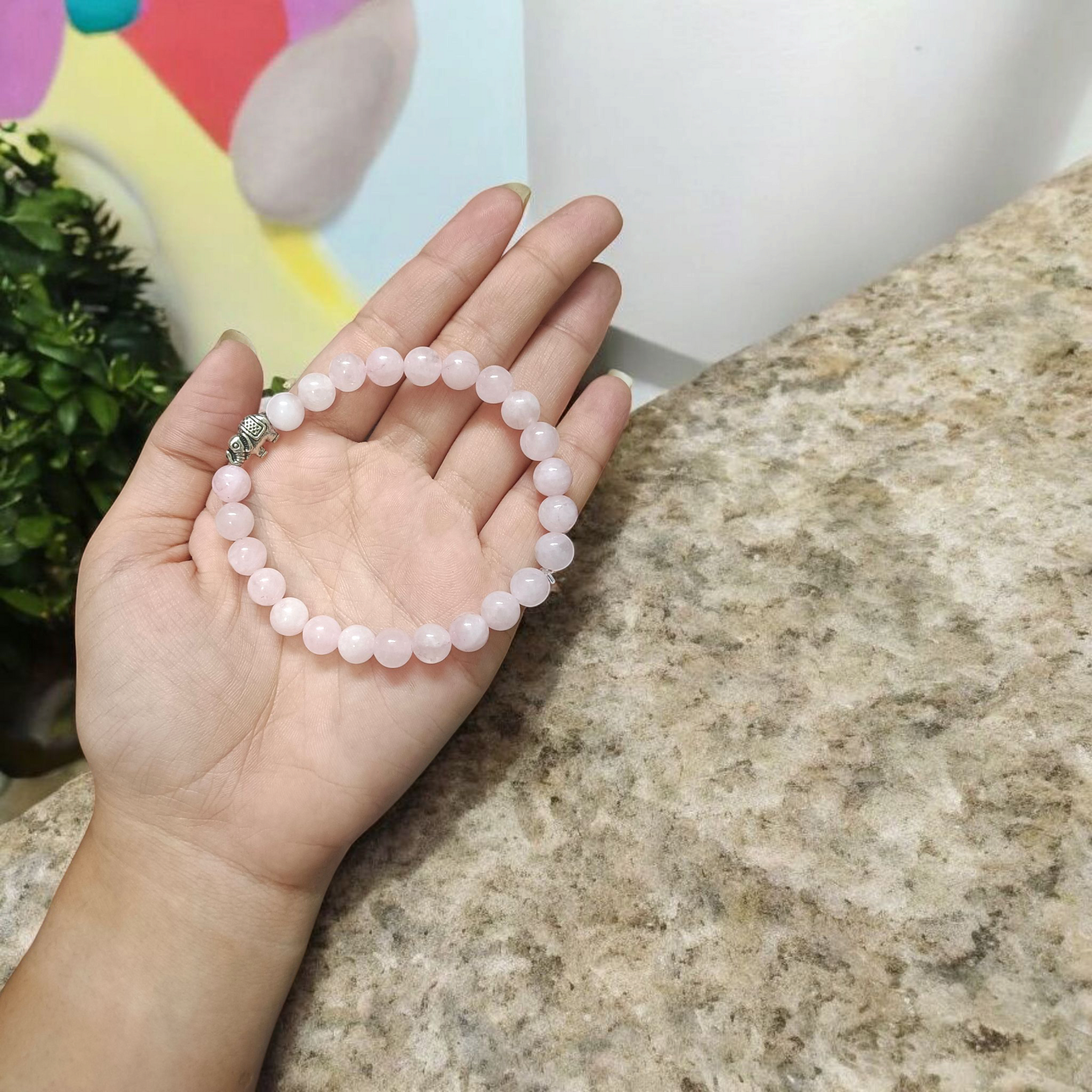 A stretchable natural rose quartz bracelet with 8mm round pink beads, displayed on a white background