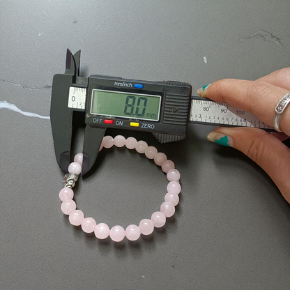 A stretchable natural rose quartz bracelet with 8mm round pink beads, displayed on a white background