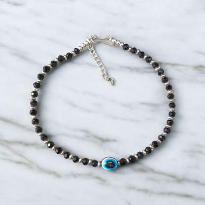 Black bead anklet for women with central evil eye charm, adjustable design for daily wear and spiritual protection by MALAWALA