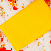 Bright yellow cotton cloth neatly folded and placed on a wooden surface for pooja and religious use