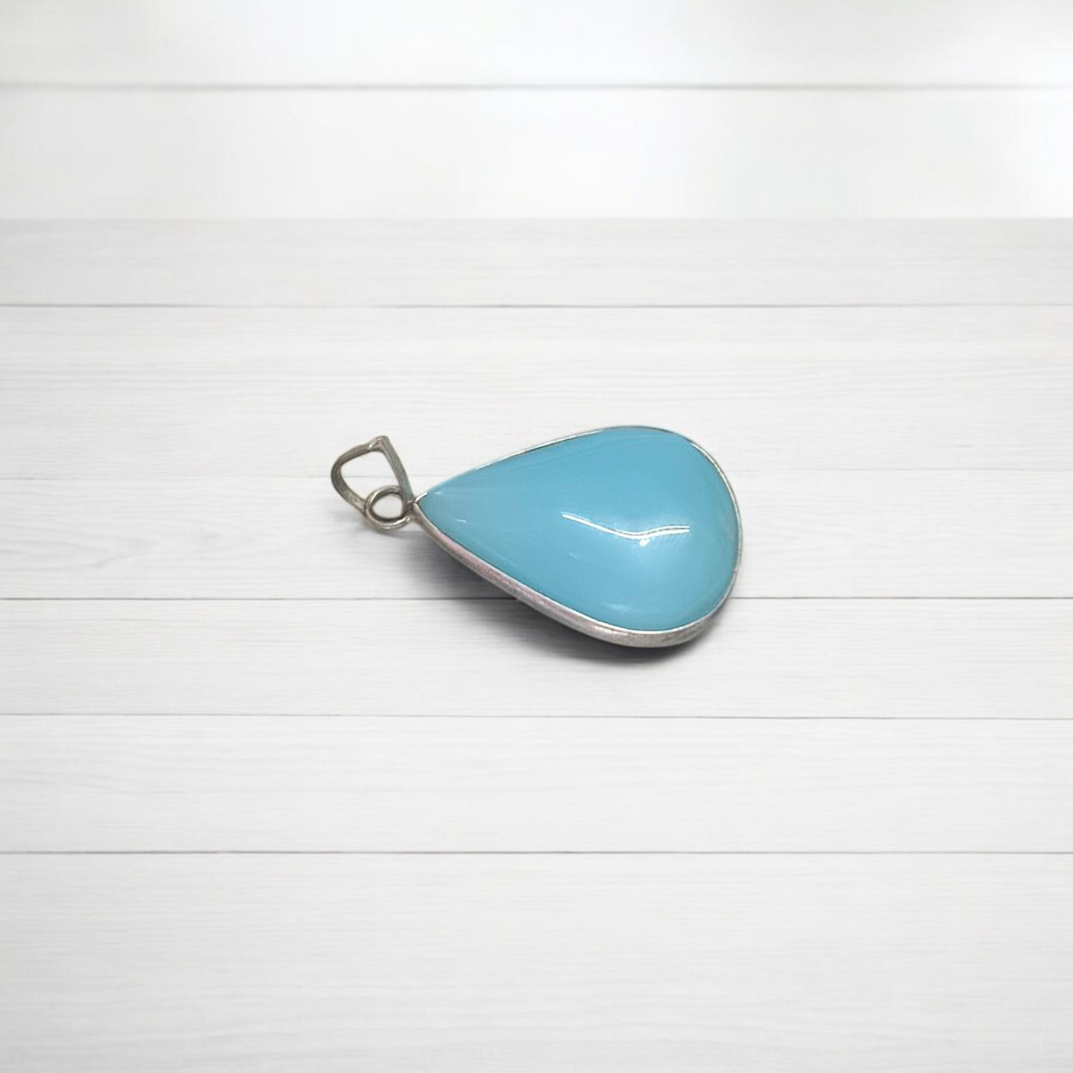 Close-up image of a natural Turquoise (Firoza) gemstone pendant with polished surface, paired with a black adjustable thread, displayed on a wooden background