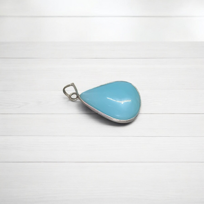 Close-up image of a natural Turquoise (Firoza) gemstone pendant with polished surface, paired with a black adjustable thread, displayed on a wooden background