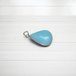 Close-up image of a natural Turquoise (Firoza) gemstone pendant with polished surface, paired with a black adjustable thread, displayed on a wooden background