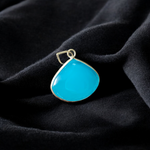 Close-up image of a natural Turquoise (Firoza) gemstone pendant with polished surface, paired with a black adjustable thread, displayed on a wooden background