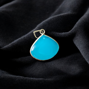 Close-up image of a natural Turquoise (Firoza) gemstone pendant with polished surface, paired with a black adjustable thread, displayed on a wooden background