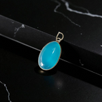 Close-up image of a natural Turquoise (Firoza) gemstone pendant with polished surface, paired with a black adjustable thread, displayed on a wooden background