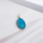 Close-up image of a natural Turquoise (Firoza) gemstone pendant with polished surface, paired with a black adjustable thread, displayed on a wooden background