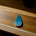 Close-up image of a natural Turquoise (Firoza) gemstone pendant with polished surface, paired with a black adjustable thread, displayed on a wooden background