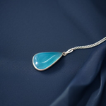 Close-up image of a natural Turquoise (Firoza) gemstone pendant with polished surface, paired with a black adjustable thread, displayed on a wooden background