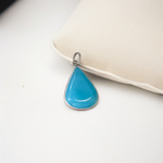 Close-up image of a natural Turquoise (Firoza) gemstone pendant with polished surface, paired with a black adjustable thread, displayed on a wooden background
