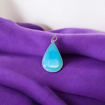 Close-up image of a natural Turquoise (Firoza) gemstone pendant with polished surface, paired with a black adjustable thread, displayed on a wooden background