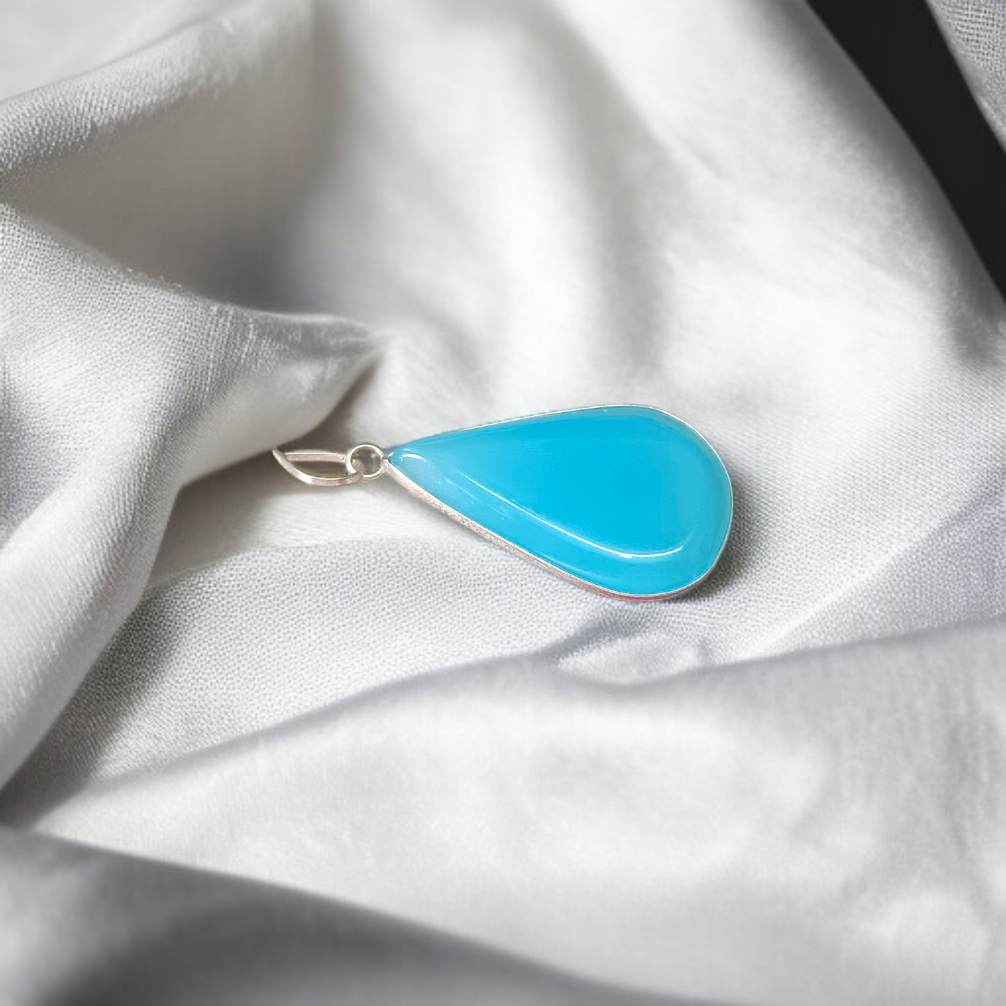 Close-up image of a natural Turquoise (Firoza) gemstone pendant with polished surface, paired with a black adjustable thread, displayed on a wooden background