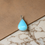 Close-up image of a natural Turquoise (Firoza) gemstone pendant with polished surface, paired with a black adjustable thread, displayed on a wooden background