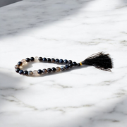 Close-up of Natural Sulemani Hakik Mala with 27+1 round 8mm black agate beads, arranged in a wrist-sized loop on a white background