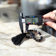 Close-up of Natural Sulemani Hakik Mala with 27+1 round 8mm black agate beads, arranged in a wrist-sized loop on a white background