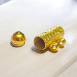 Five golden metal cylindrical taweez neatly arranged with Bhojpatra sheets on a clean white surface