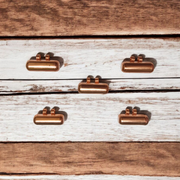 Five handcrafted cylindrical copper taweez placed beside Bhojpatra sheets on a clean, white background