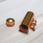 Five handcrafted cylindrical copper taweez placed beside Bhojpatra sheets on a clean, white background