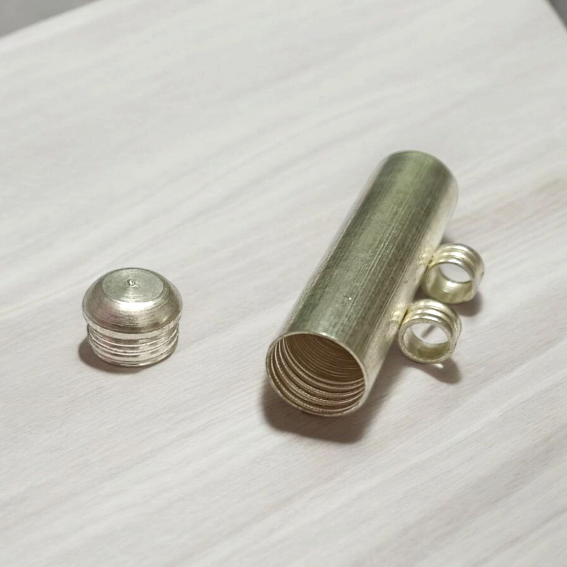 Five silver-plated cylindrical taweez amulets with accompanying Bhojpatra sheets placed neatly on a white surface