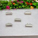 Five silver-plated cylindrical taweez amulets with accompanying Bhojpatra sheets placed neatly on a white surface