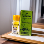 Glass bottle of 2ML Chameli Attar by Veena, adorned with a golden cap and floral-themed label, surrounded by jasmine flowers on a wooden surface