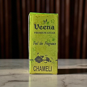 Glass bottle of 2ML Chameli Attar by Veena, adorned with a golden cap and floral-themed label, surrounded by jasmine flowers on a wooden surface