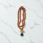 Gold-wired Rudraksha mala with 8mm beads, featuring a silver-tone Trishul pendant, arranged neatly on a dark wooden background