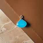 Close-up image of a natural Turquoise (Firoza) gemstone pendant with polished surface, paired with a black adjustable thread, displayed on a wooden background